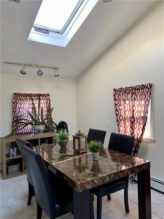 dining area featuring track lighting, a baseboard radiator, light tile patterned floors, and a skylight