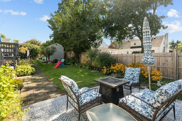 view of patio / terrace with a storage shed, an outbuilding, a fenced backyard, and an outdoor fire pit