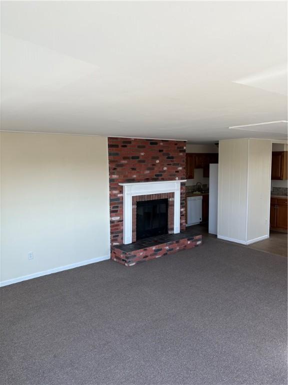 unfurnished living room featuring a brick fireplace, baseboards, and dark colored carpet
