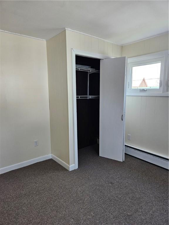unfurnished bedroom with a closet, baseboards, a baseboard heating unit, and dark colored carpet