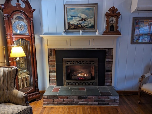 sitting room with a brick fireplace, a wall unit AC, and hardwood / wood-style flooring