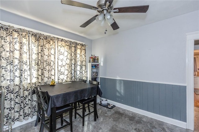 dining space with ceiling fan and wood walls