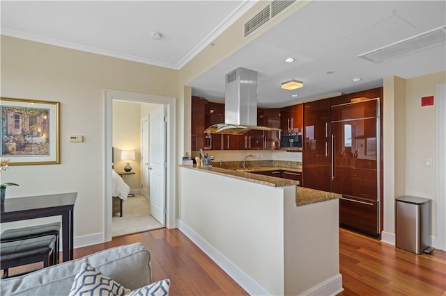 kitchen with light stone counters, kitchen peninsula, dark hardwood / wood-style flooring, and island exhaust hood