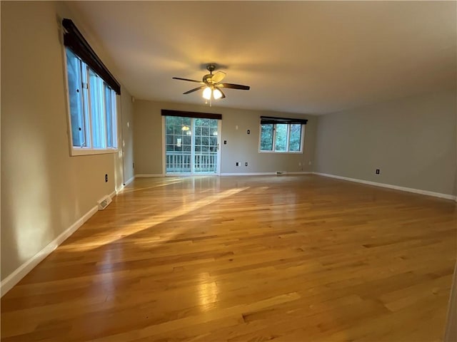 empty room with ceiling fan, a wealth of natural light, and light wood-type flooring