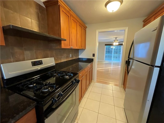 kitchen with light tile patterned floors, refrigerator, dark stone counters, and stainless steel gas range oven