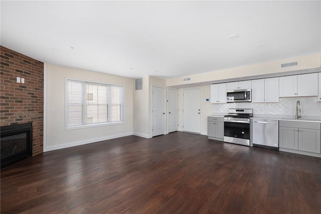 kitchen featuring dark hardwood / wood-style flooring, stainless steel appliances, a fireplace, sink, and backsplash