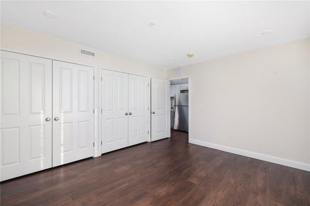 unfurnished bedroom featuring multiple closets, stainless steel fridge, and dark hardwood / wood-style floors