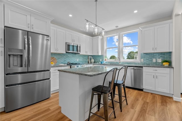 kitchen with light stone countertops, appliances with stainless steel finishes, a center island, white cabinetry, and light wood-type flooring