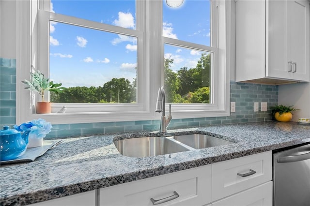 kitchen featuring stainless steel dishwasher, white cabinets, sink, and stone counters