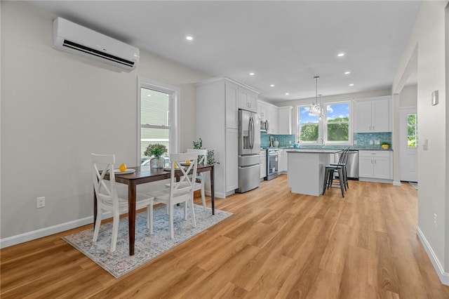 kitchen featuring decorative light fixtures, a wall unit AC, a kitchen island, stainless steel appliances, and white cabinets