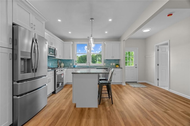 kitchen featuring decorative light fixtures, a center island, white cabinetry, a kitchen breakfast bar, and stainless steel appliances