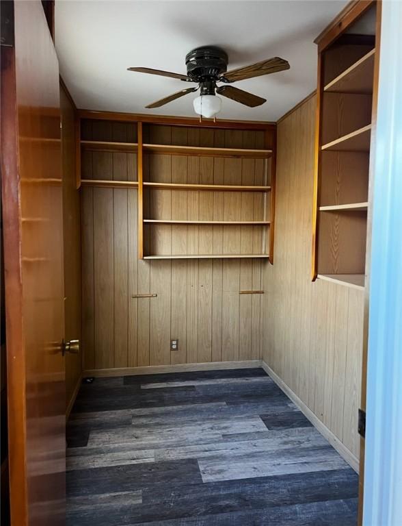 empty room featuring ceiling fan, built in shelves, dark hardwood / wood-style flooring, and wooden walls