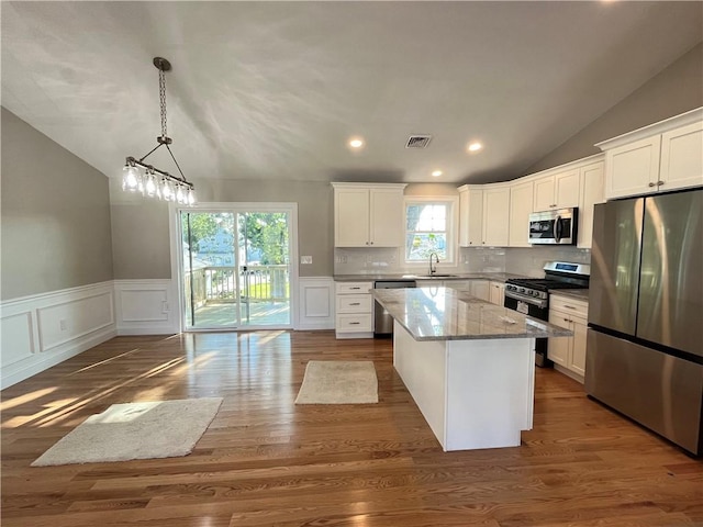 kitchen with appliances with stainless steel finishes, white cabinetry, decorative light fixtures, and a center island