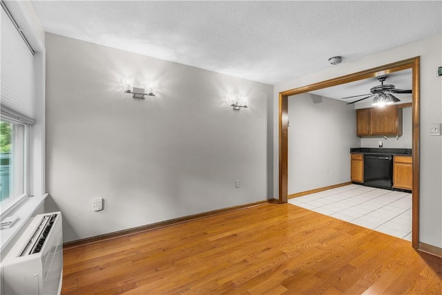 unfurnished living room featuring light wood-type flooring, a textured ceiling, a wall mounted AC, and ceiling fan