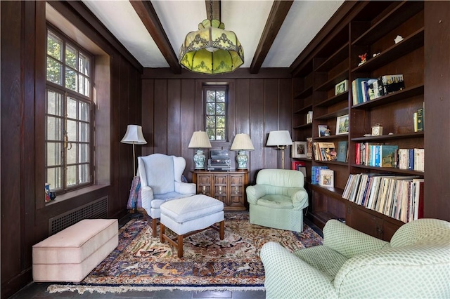 living area featuring built in shelves, beamed ceiling, a healthy amount of sunlight, and wood walls