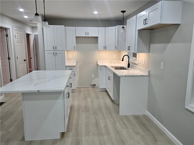 kitchen with light stone countertops, white cabinets, a kitchen island, decorative light fixtures, and sink