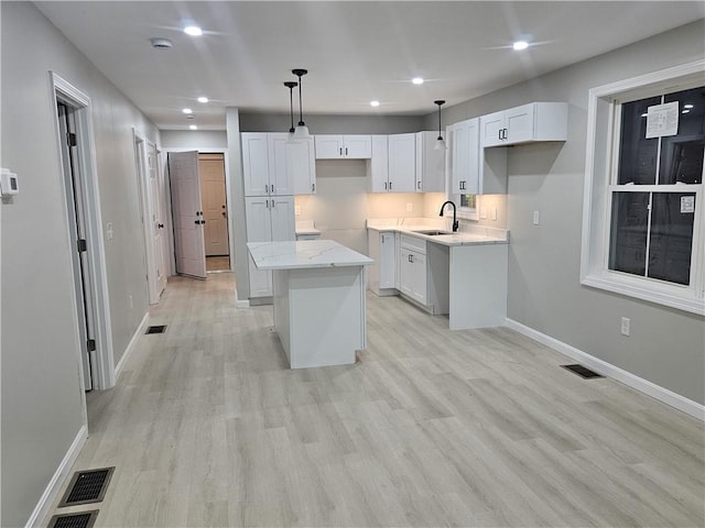 kitchen featuring hanging light fixtures, sink, white cabinetry, and a center island