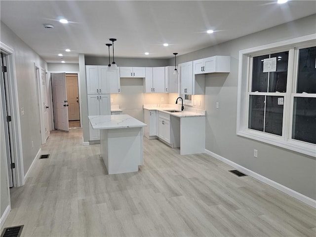 kitchen featuring decorative light fixtures, white cabinets, light stone counters, and a kitchen island