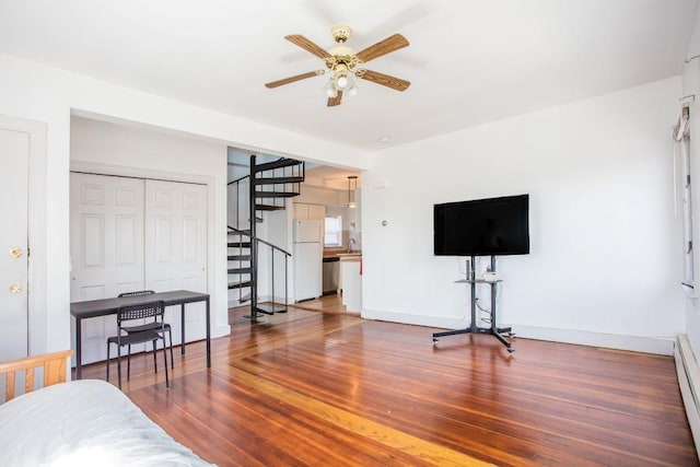 bedroom featuring wood-type flooring, a baseboard heating unit, white refrigerator, a closet, and ceiling fan