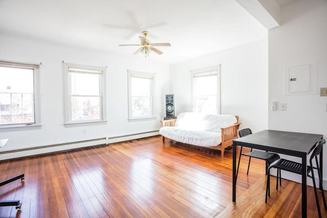 living area featuring baseboard heating, electric panel, hardwood / wood-style flooring, and ceiling fan