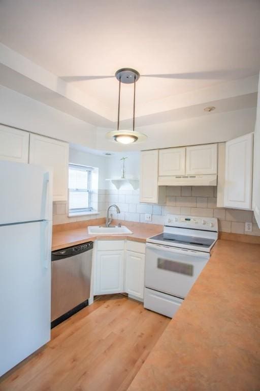 kitchen featuring white appliances, white cabinetry, sink, hanging light fixtures, and light hardwood / wood-style flooring