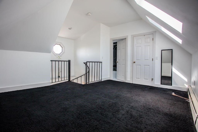 bonus room featuring vaulted ceiling with skylight, a baseboard heating unit, and dark colored carpet