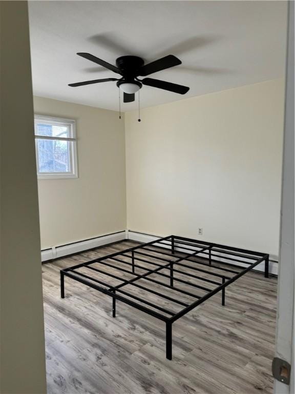 unfurnished bedroom with ceiling fan, a baseboard heating unit, and light hardwood / wood-style floors