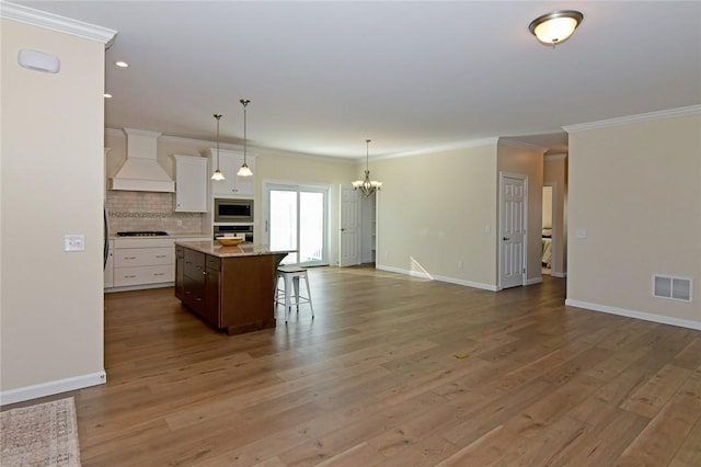 kitchen with backsplash, a kitchen island, custom exhaust hood, stainless steel appliances, and white cabinets