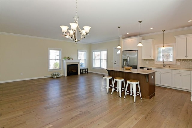 kitchen with a center island, white cabinetry, sink, stainless steel fridge with ice dispenser, and a breakfast bar area