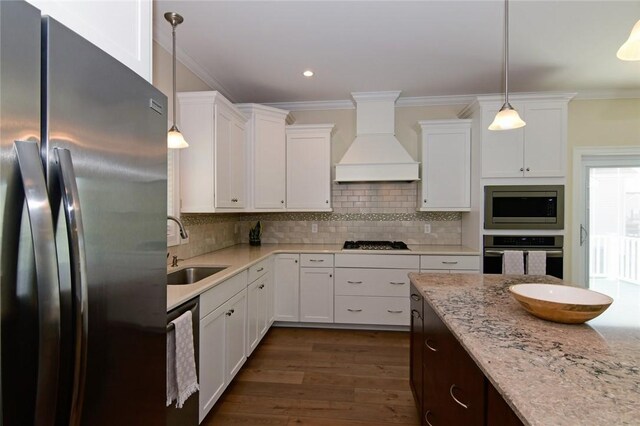 kitchen with premium range hood, appliances with stainless steel finishes, white cabinets, light stone counters, and sink