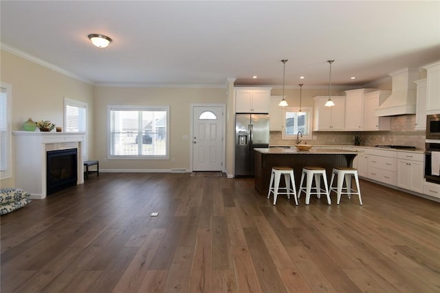 kitchen with a center island, a kitchen bar, white cabinetry, appliances with stainless steel finishes, and custom range hood