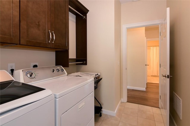 laundry room featuring washing machine and dryer, light tile patterned flooring, and cabinets