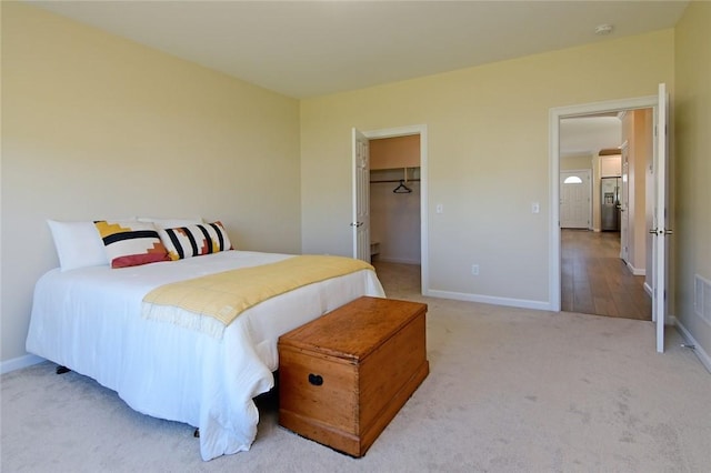 bedroom with stainless steel refrigerator with ice dispenser, a closet, a walk in closet, and carpet flooring