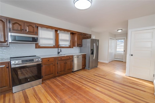 kitchen with a baseboard heating unit, appliances with stainless steel finishes, backsplash, light wood-type flooring, and sink