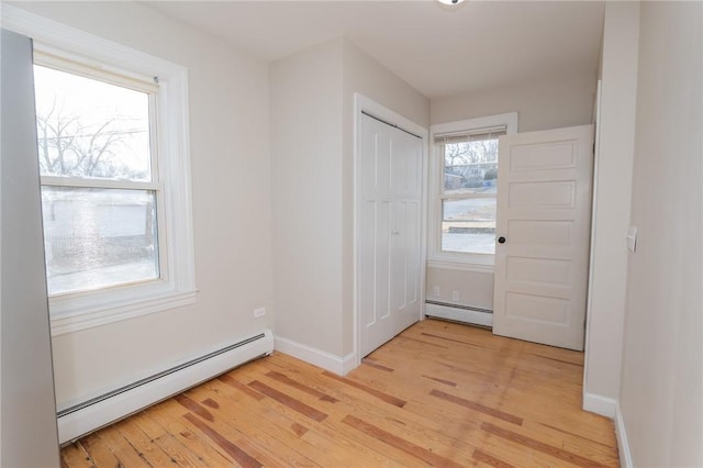 interior space with a baseboard heating unit, a closet, and light hardwood / wood-style flooring