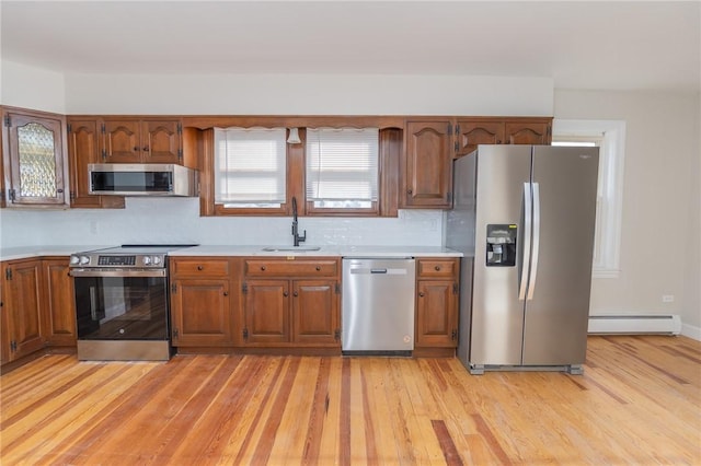 kitchen with tasteful backsplash, a baseboard heating unit, sink, light wood-type flooring, and appliances with stainless steel finishes