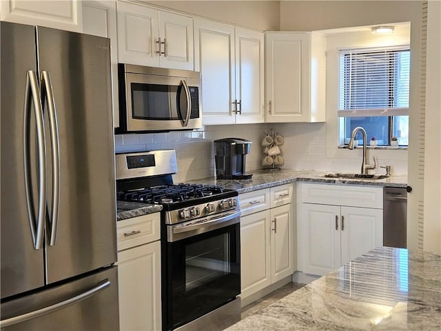 kitchen with backsplash, sink, white cabinetry, light stone countertops, and appliances with stainless steel finishes