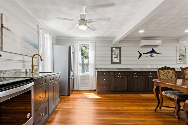 kitchen featuring an AC wall unit, dark brown cabinetry, stainless steel appliances, light stone countertops, and beam ceiling