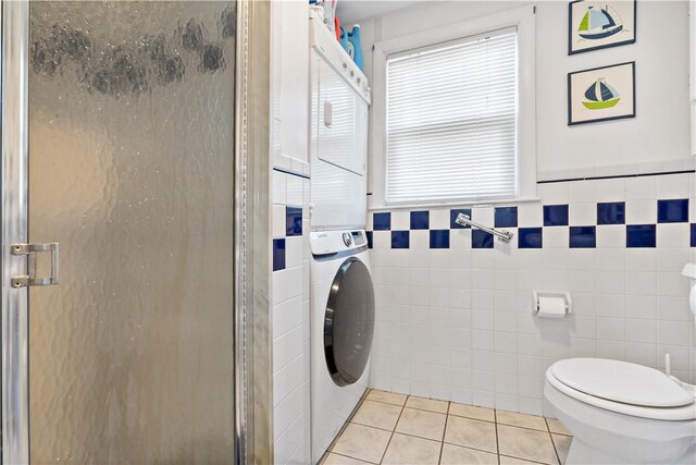 bathroom featuring stacked washer and clothes dryer, tile patterned flooring, tile walls, and a shower with door