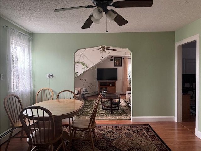 dining room featuring ceiling fan, wood-type flooring, a textured ceiling, and a baseboard heating unit