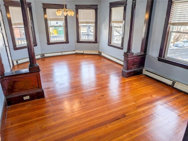 empty room with an inviting chandelier, hardwood / wood-style floors, decorative columns, and a baseboard heating unit