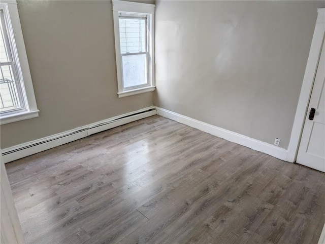 unfurnished room featuring a healthy amount of sunlight, a baseboard heating unit, and light hardwood / wood-style floors