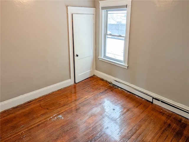 empty room with hardwood / wood-style flooring and a baseboard heating unit