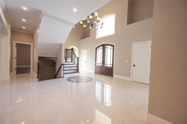 foyer entrance with french doors, a towering ceiling, a chandelier, and ornamental molding