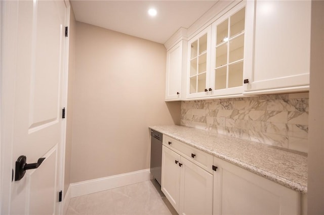 interior space with tasteful backsplash, stainless steel dishwasher, light tile patterned flooring, white cabinetry, and light stone countertops