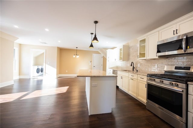 kitchen featuring decorative light fixtures, washer and dryer, light stone countertops, appliances with stainless steel finishes, and white cabinets