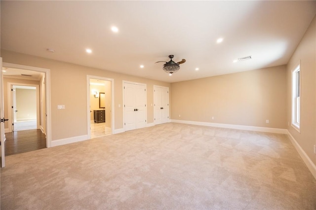 unfurnished bedroom with ceiling fan, light colored carpet, connected bathroom, and two closets