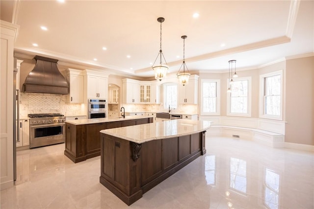 kitchen with hanging light fixtures, appliances with stainless steel finishes, a kitchen breakfast bar, an island with sink, and custom range hood