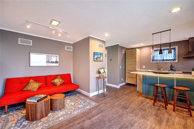 living room featuring wet bar, track lighting, hardwood / wood-style floors, and ornamental molding