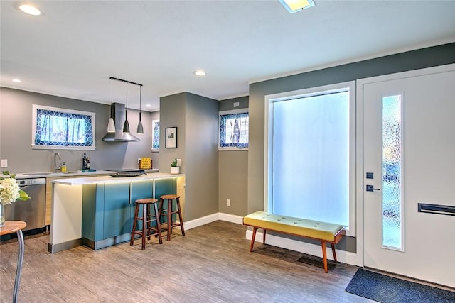 kitchen featuring pendant lighting, wall chimney range hood, wood-type flooring, sink, and stainless steel dishwasher